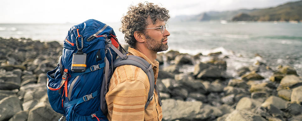 Aventureiro com SPOT Gen4 fixado à mochila em costa rochosa — rastreio GPS satelital outdoor