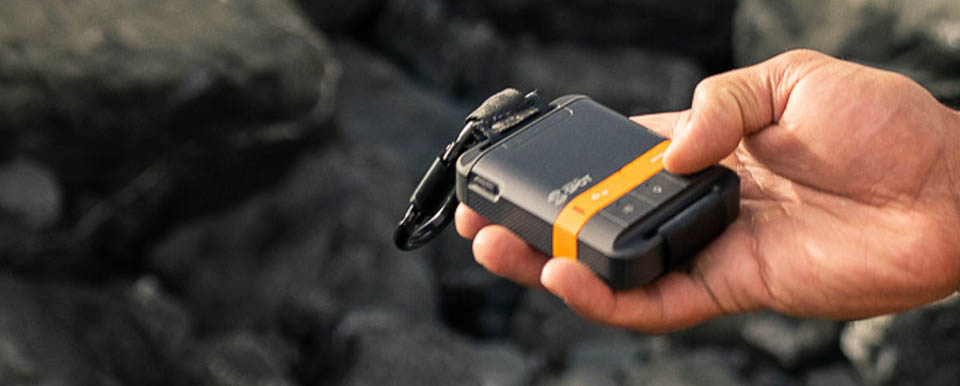 Mão segurando o SPOT Gen4 em ambiente rochoso — localizador GPS satelital compacto