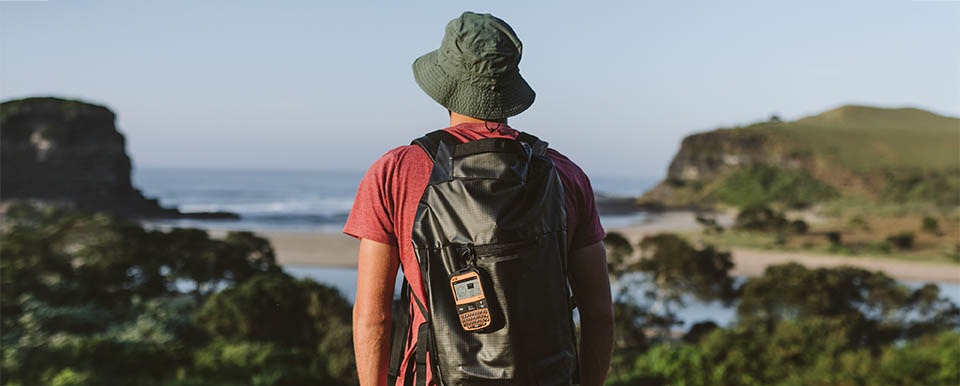 Aventureiro com SPOT X na mochila observando paisagem costeira — comunicação satelital em áreas remotas